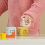 mani dinbambina con maglione rosa che gioca su un baco con dei cubi con le lettere