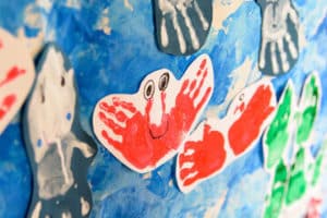 disefi attaccati su una parete colorata di celeste di impronte di manine che formano un granchio rosso