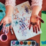 mani di bambina colorate su un baco con fogli con impronte e acquerelli